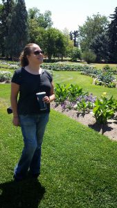 Liv Leigh standing in a beautiful garden, wearing sunglasses, jeans, and a black tshirt, smiling while looking off in the distance.